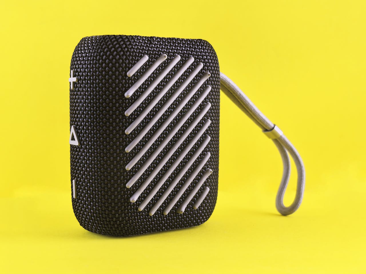 Black portable Bluetooth speaker with strap on a bright yellow backdrop, showcasing modern design.